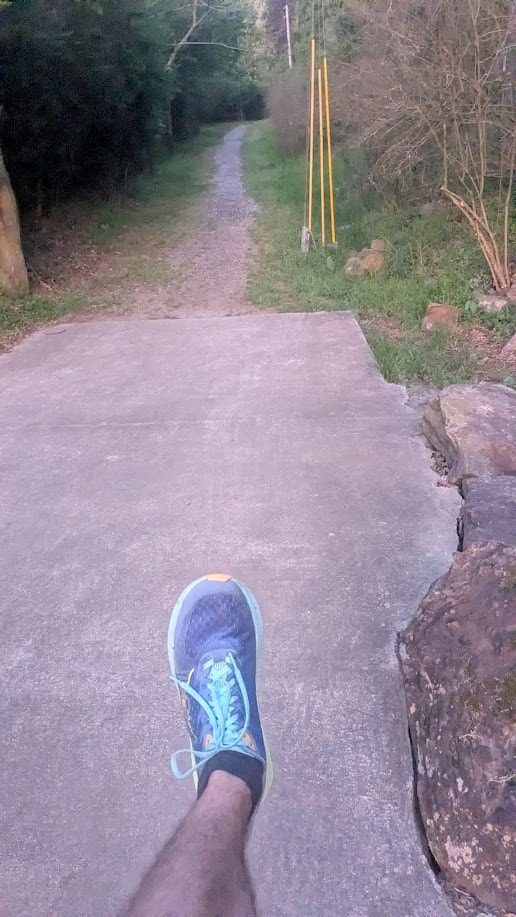 Looking down at running shoes on a paved trail heading into the woods